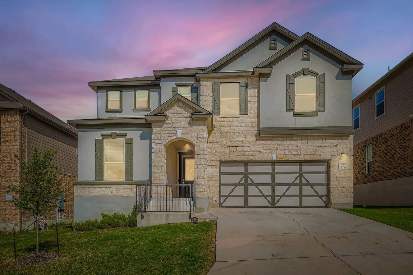Two-story San Antonio house with stone and siding, a double garage and a front lawn beneath a pink sky