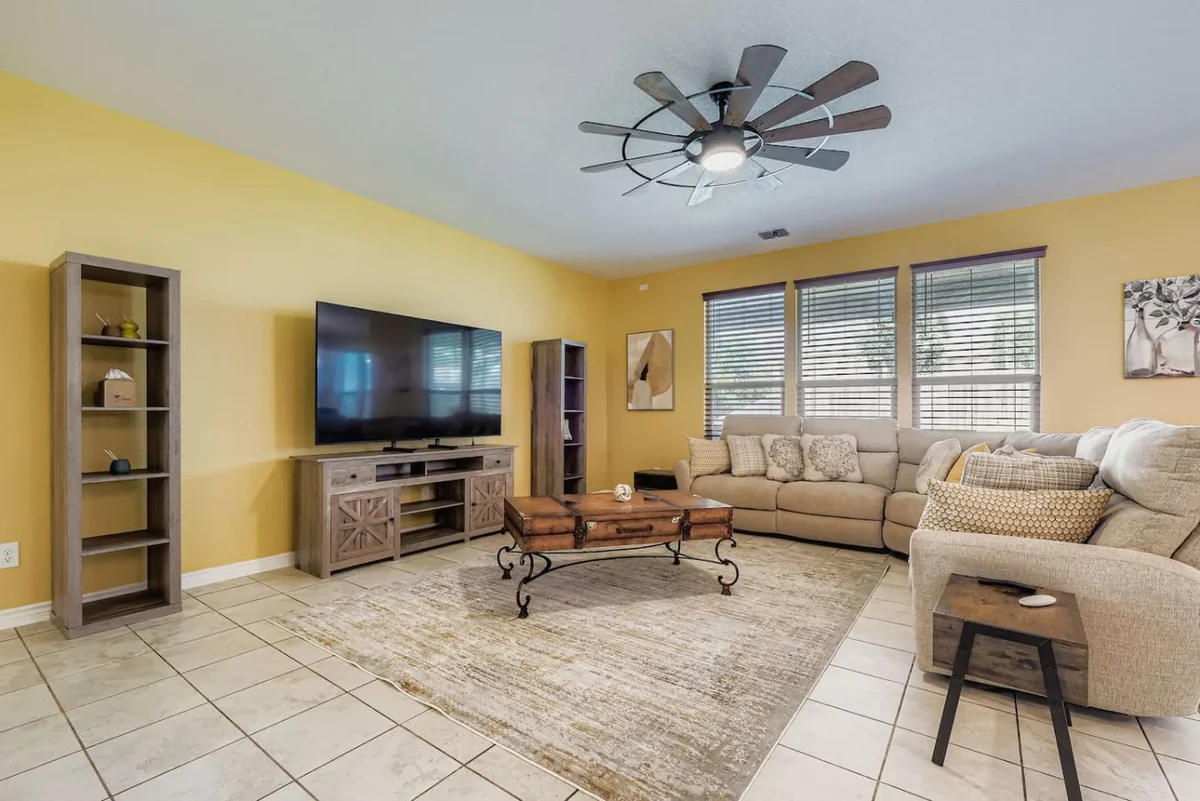 Yellow living room with beige sectional seating, a wall-mounted television and a ceiling fan