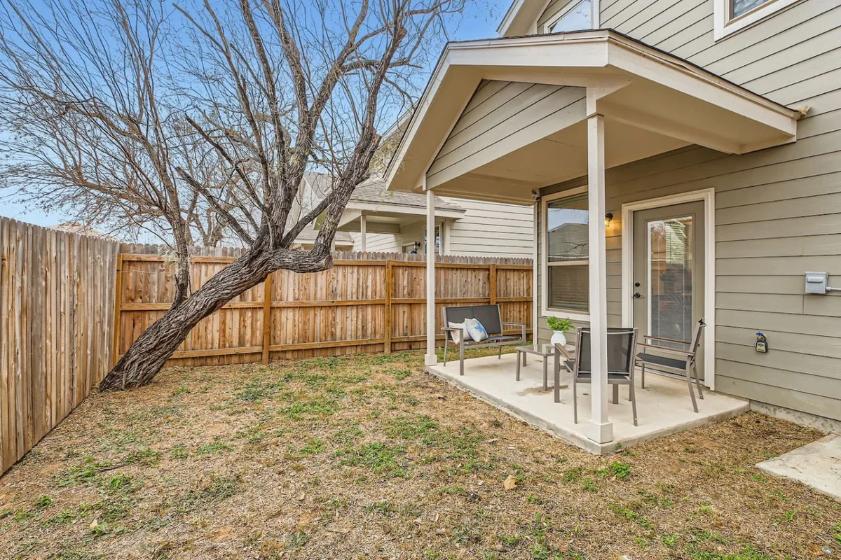 Fenced lawn with a leafless tree and a covered patio beside the gray duplex
